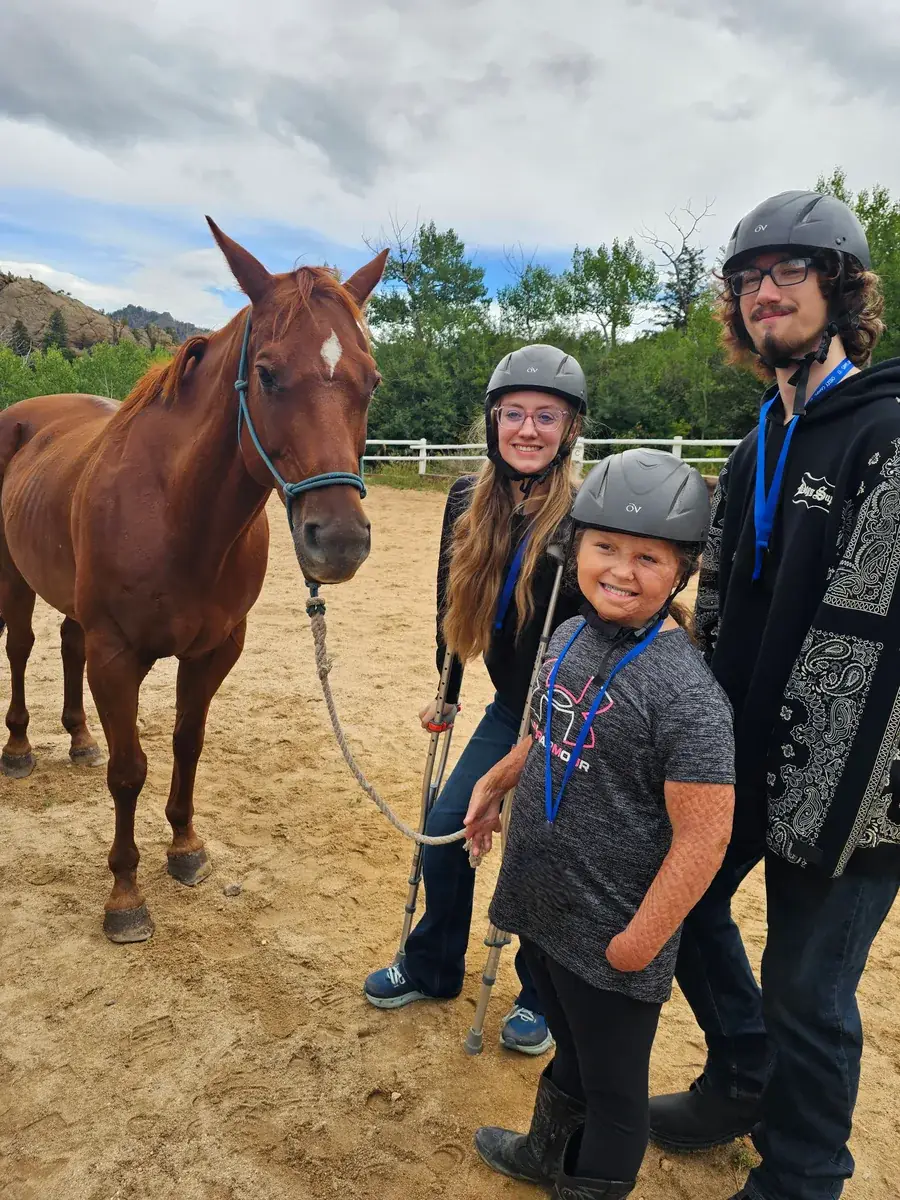 Summer Camp riders wearing helmets and standing beside a horse