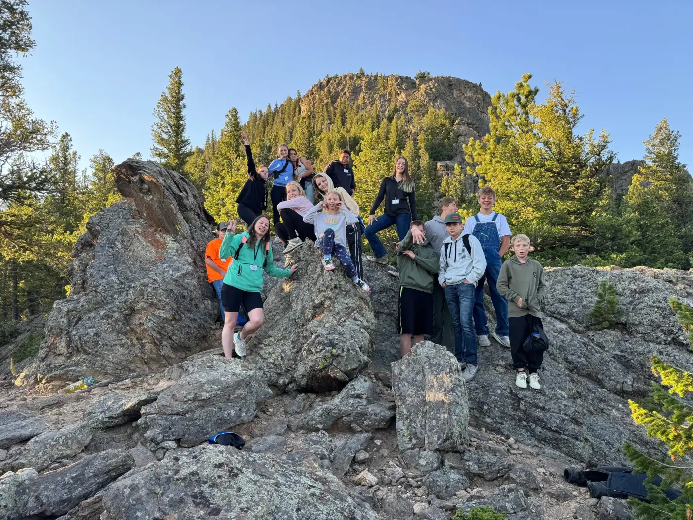 Summer Camp friends gathered on rocks beneath a forested mountain