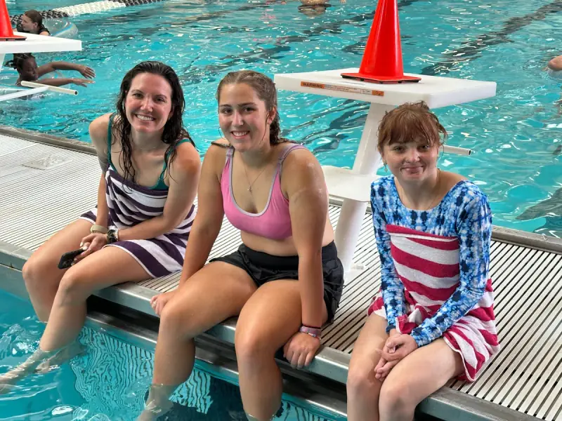 Three friends smiling together beside the swimming pool