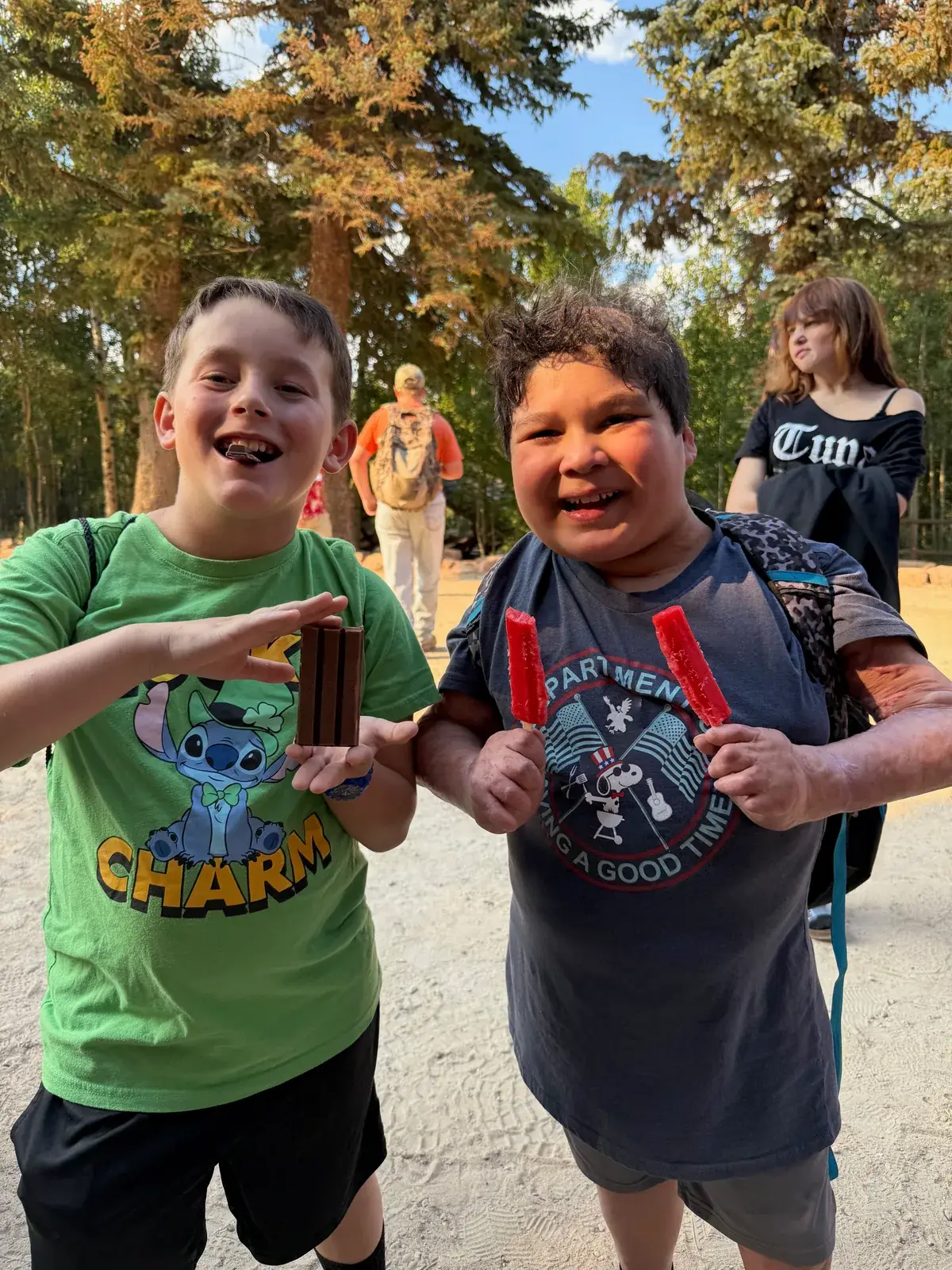 Two smiling campers enjoying frozen treats, one holding two red popsicles