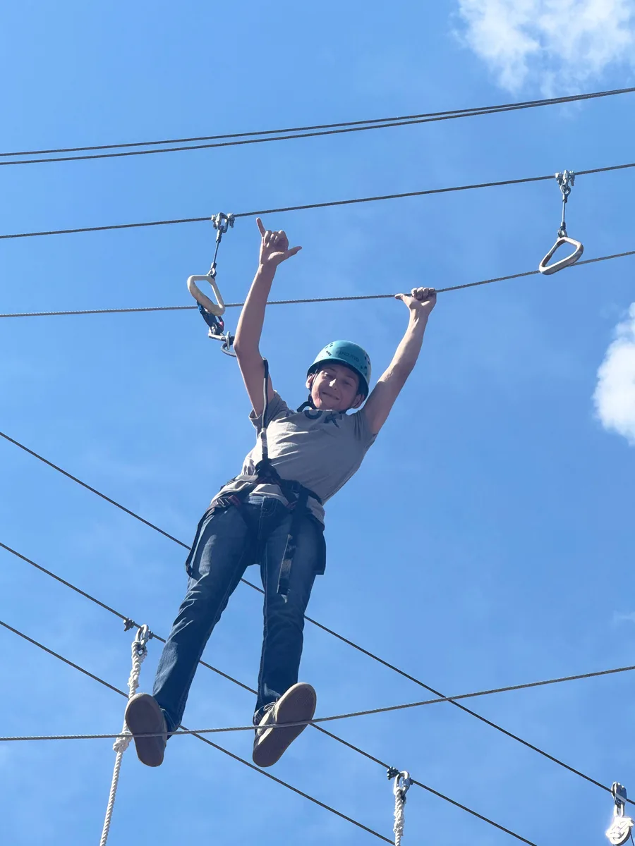 Camper wearing a safety harness and reaching for the rings on a high ropes course