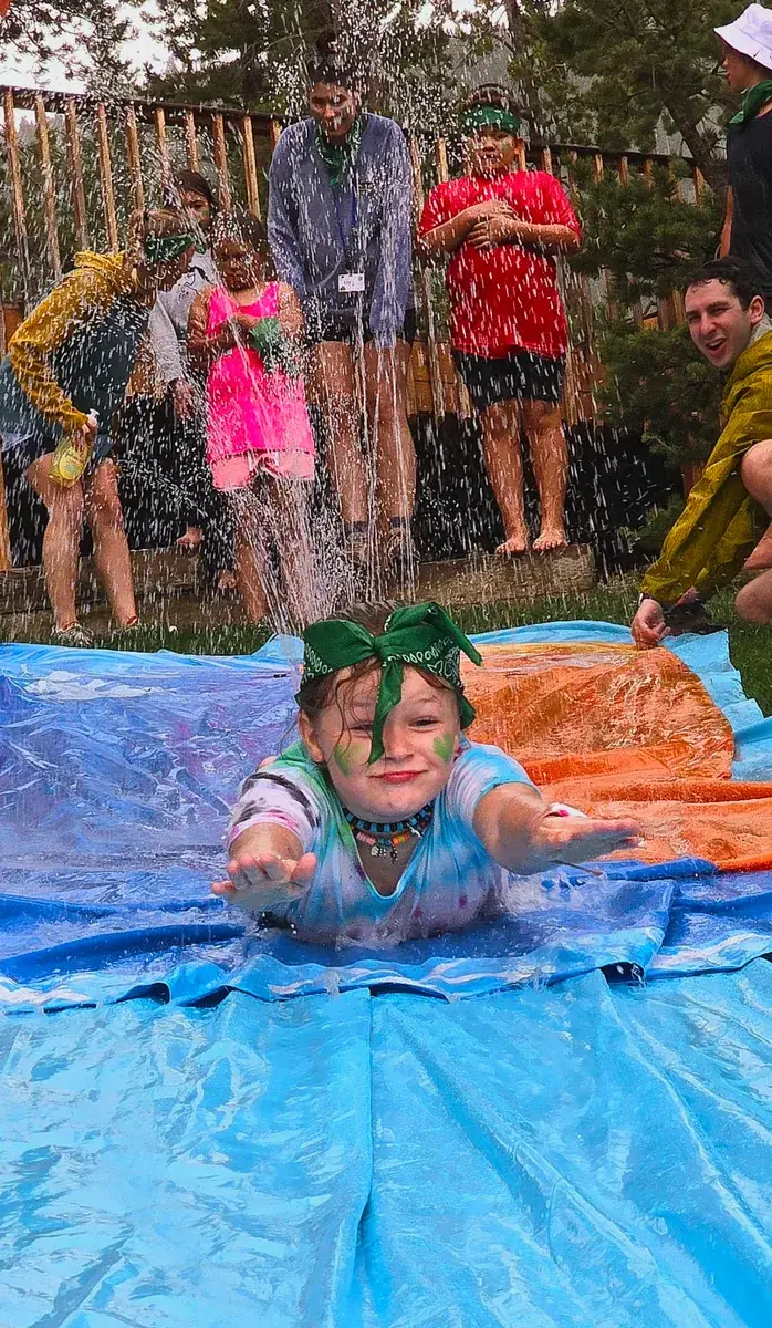 Camper sliding through a spray of water on a colorful outdoor water slide